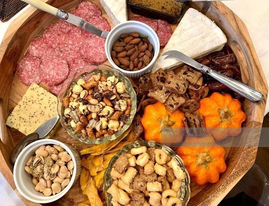 Ang isang malaking, bilog na pinggan na gawa sa kahoy ay naglalaman ng malaking hanay ng mga appetizer para sa pasasalamat.Ang platter ay naglalaman ng mga pampalamuti na kalabasa, keso, salami, pinatuyong mangga, mani, crackers, biskwit at pate